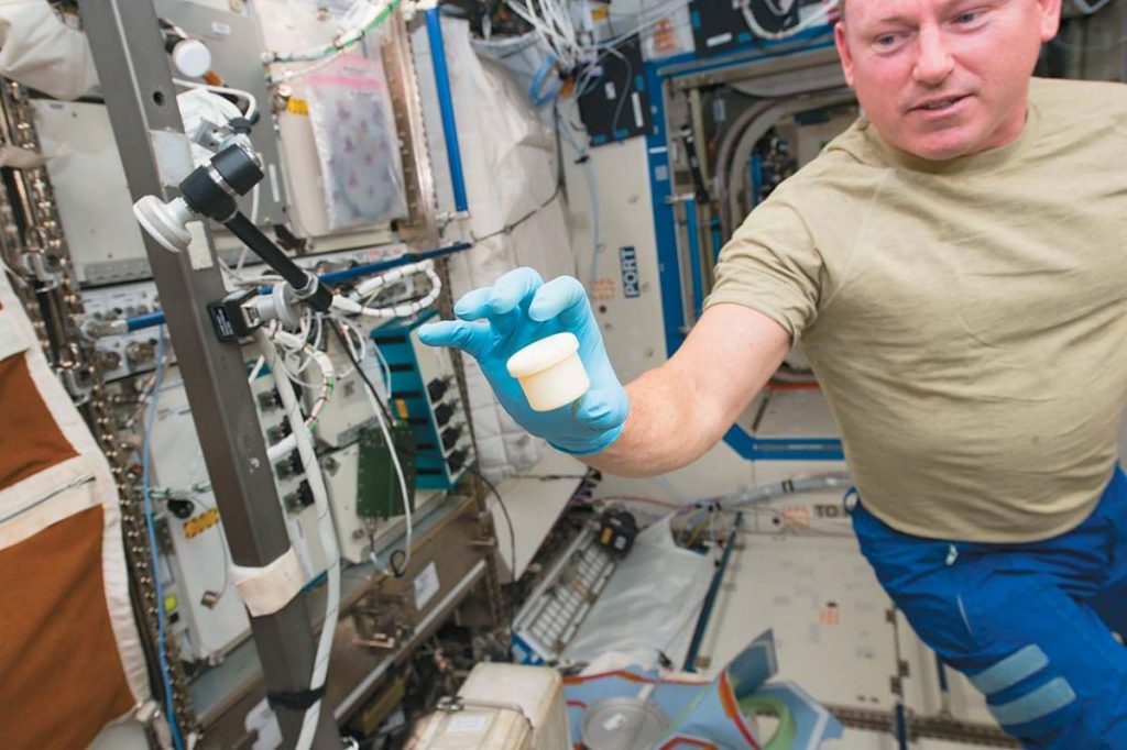 Астронавт Барри Уилмор демонстрирует один из первых предметов, напеча- танных на борту МКС на 3D-принтере, — контейнер с крышкой для хранения образцов для научных экспериментов